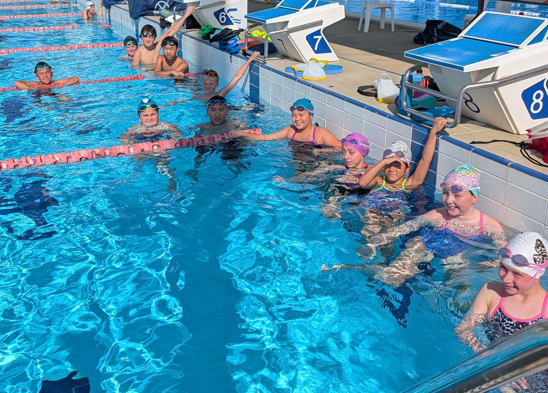 Swimmers in a pool, holding starting blocks, ready to race.