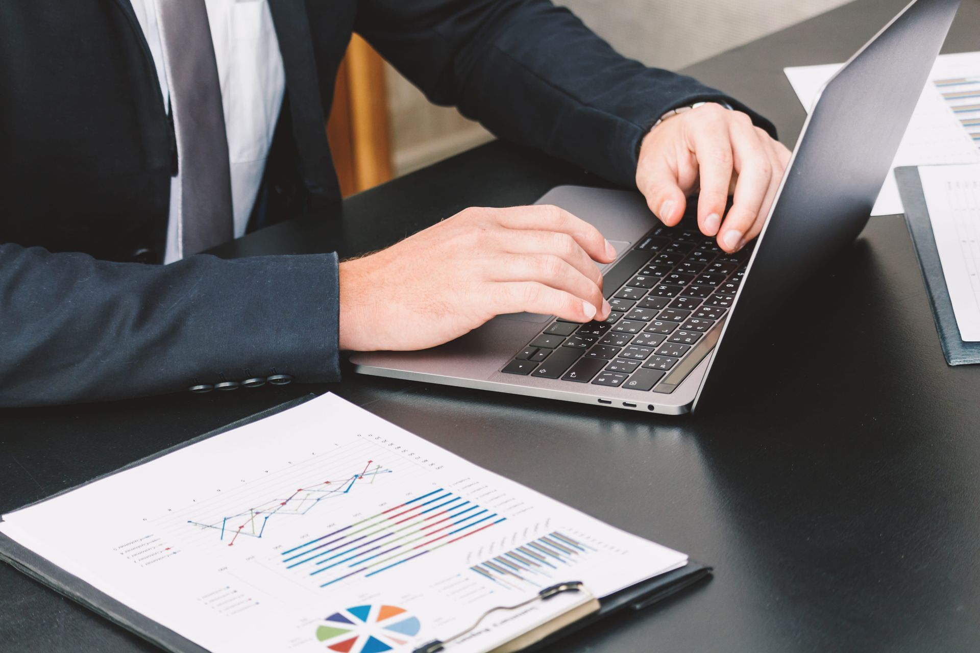 Person typing on a laptop at a desk beside a business chart report
