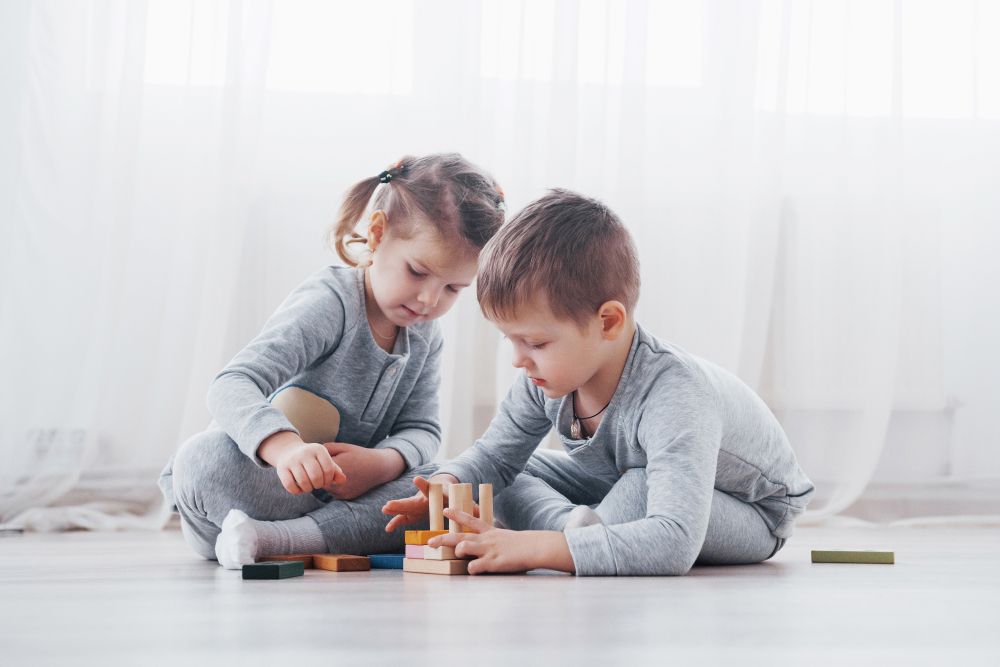 A Boy and a Girl Are Sitting on the Floor Playing With Wooden Blocks — Charmhaven Carpets In Charmhaven, NSW