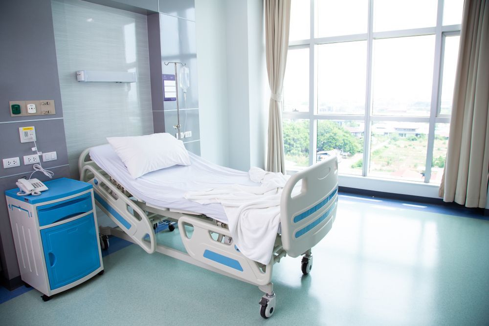 An Empty Hospital Room With a Bed, Nightstand, and Window — Charmhaven Carpets In Charmhaven, NSW