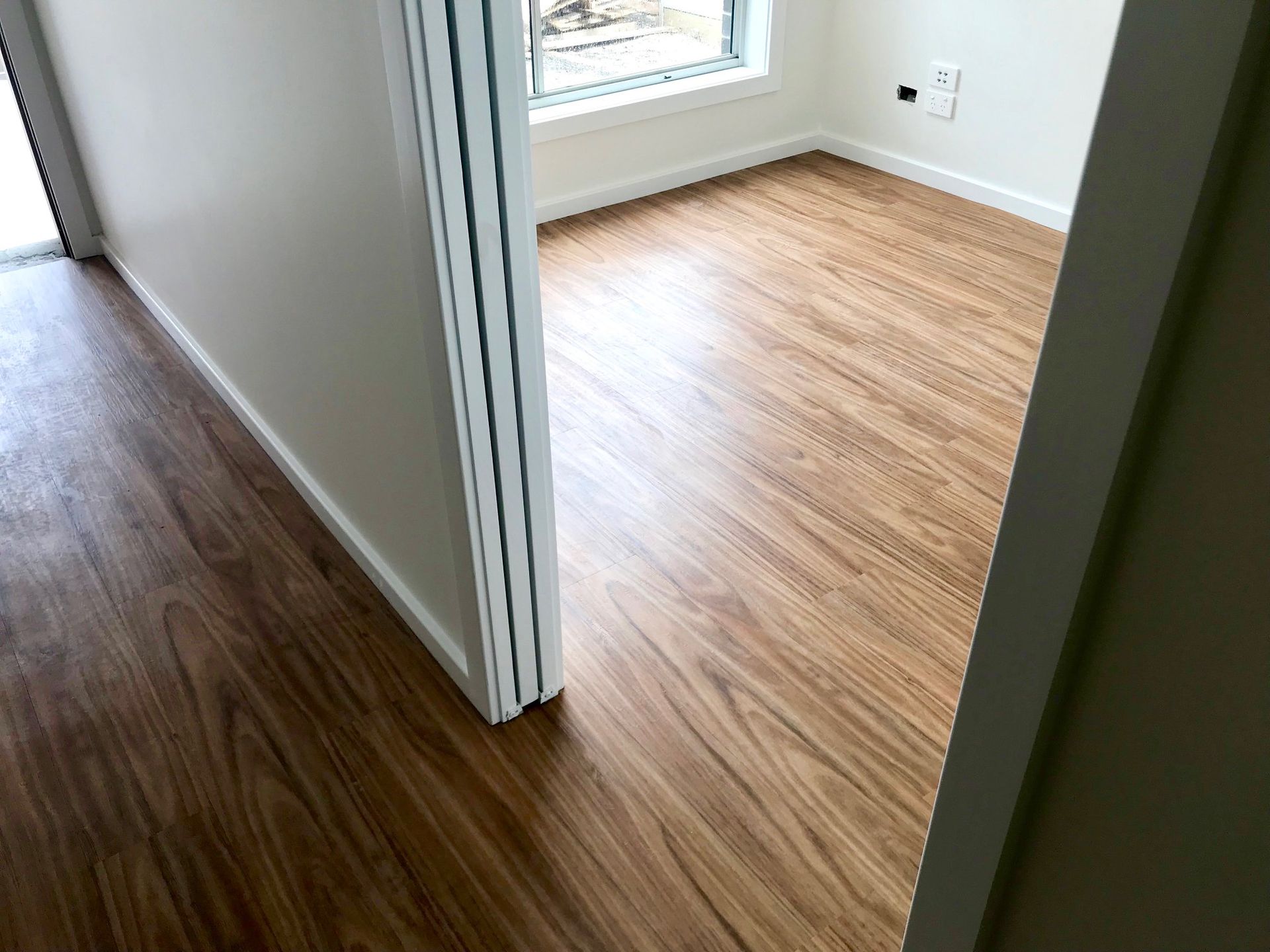 Hallway with Wood Flooring Leading Into a Bright Empty Room — Charmhaven Carpets In Charmhaven, NSW