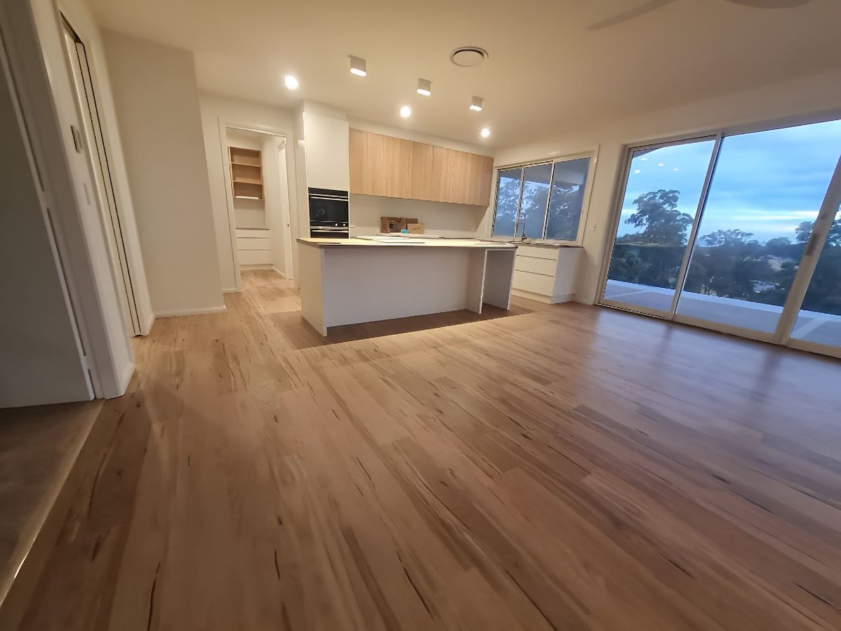 A Living Room With Hardwood Floors And A Kitchen With Sliding Glass Doors — Charmhaven Carpets In Charmhaven, NSW