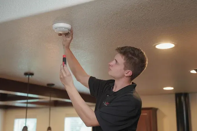Man installing a smoke detector on the ceiling with a screwdriver