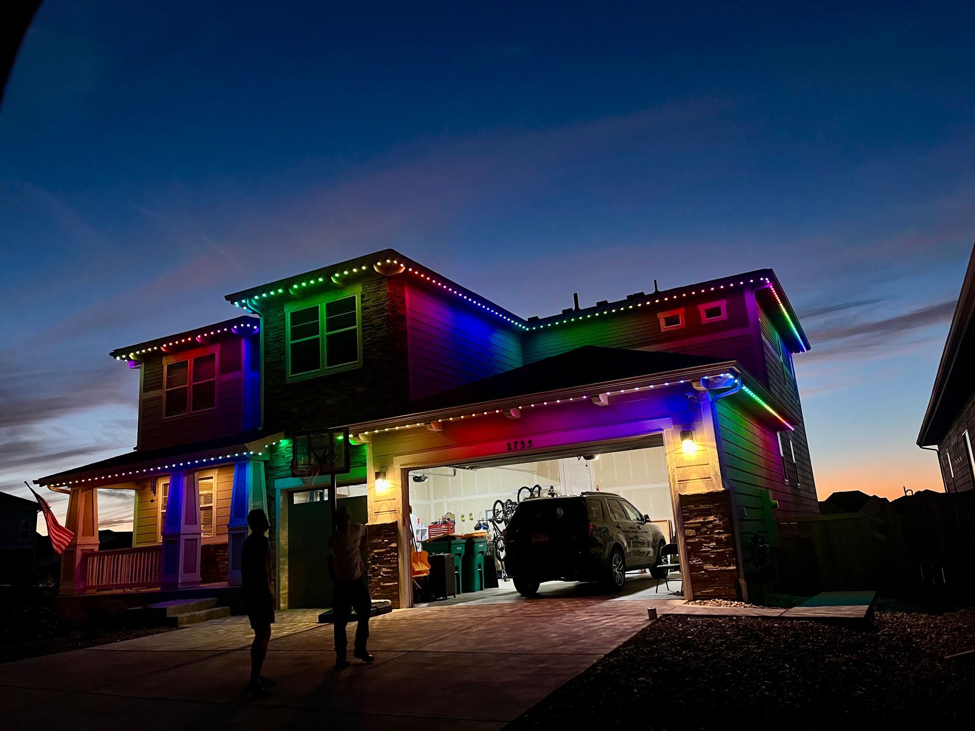 Two-story house with colorful Christmas lights at dusk and a car parked in the driveway