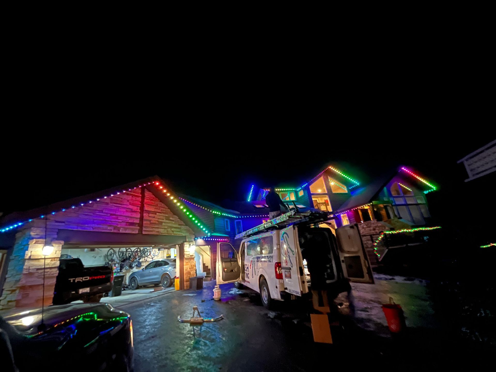 Rainbow-lit house and fire truck at night, with a driveway wet from rain.