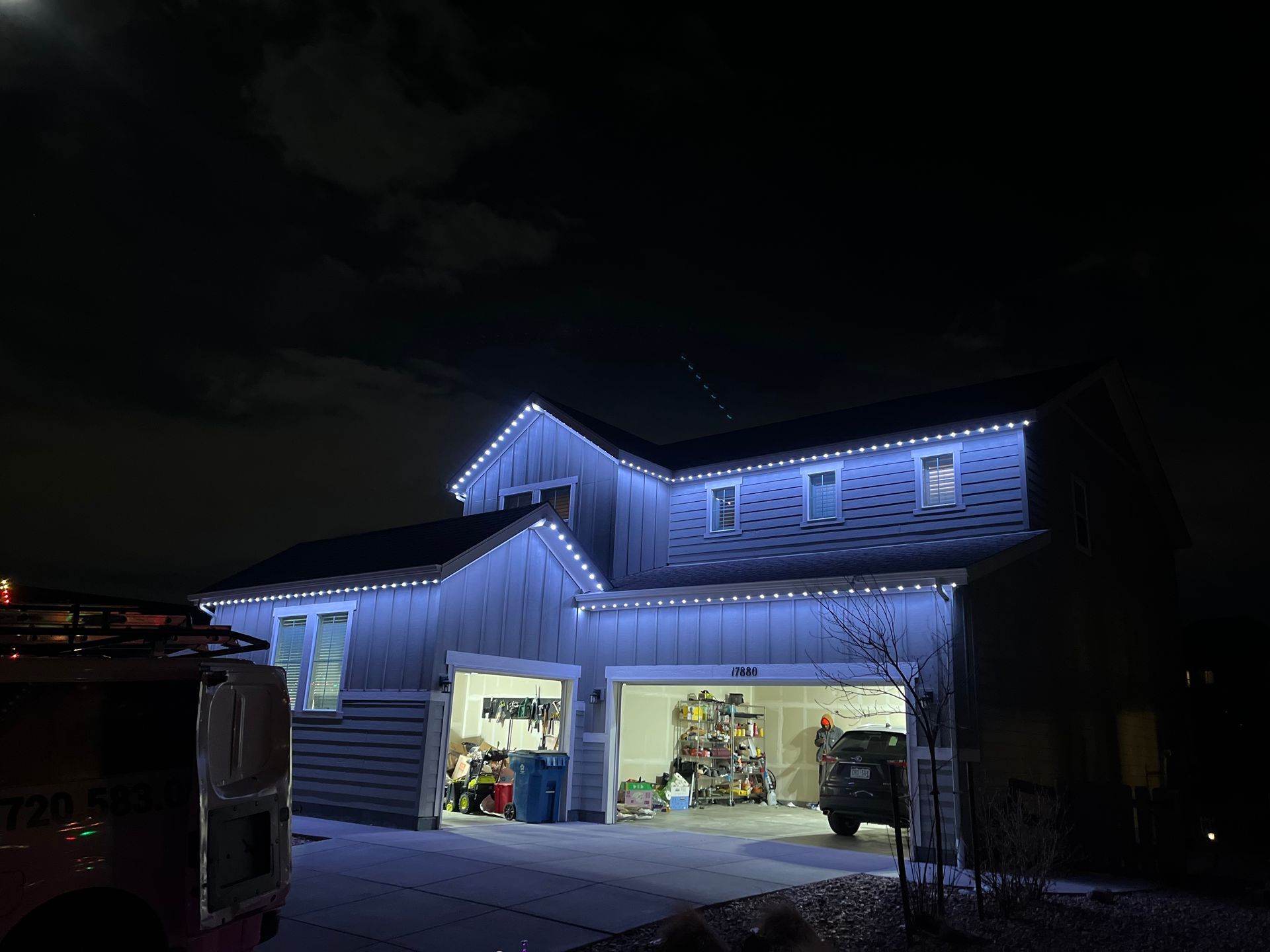 Blue-lit house at night with open garage and vehicles inside