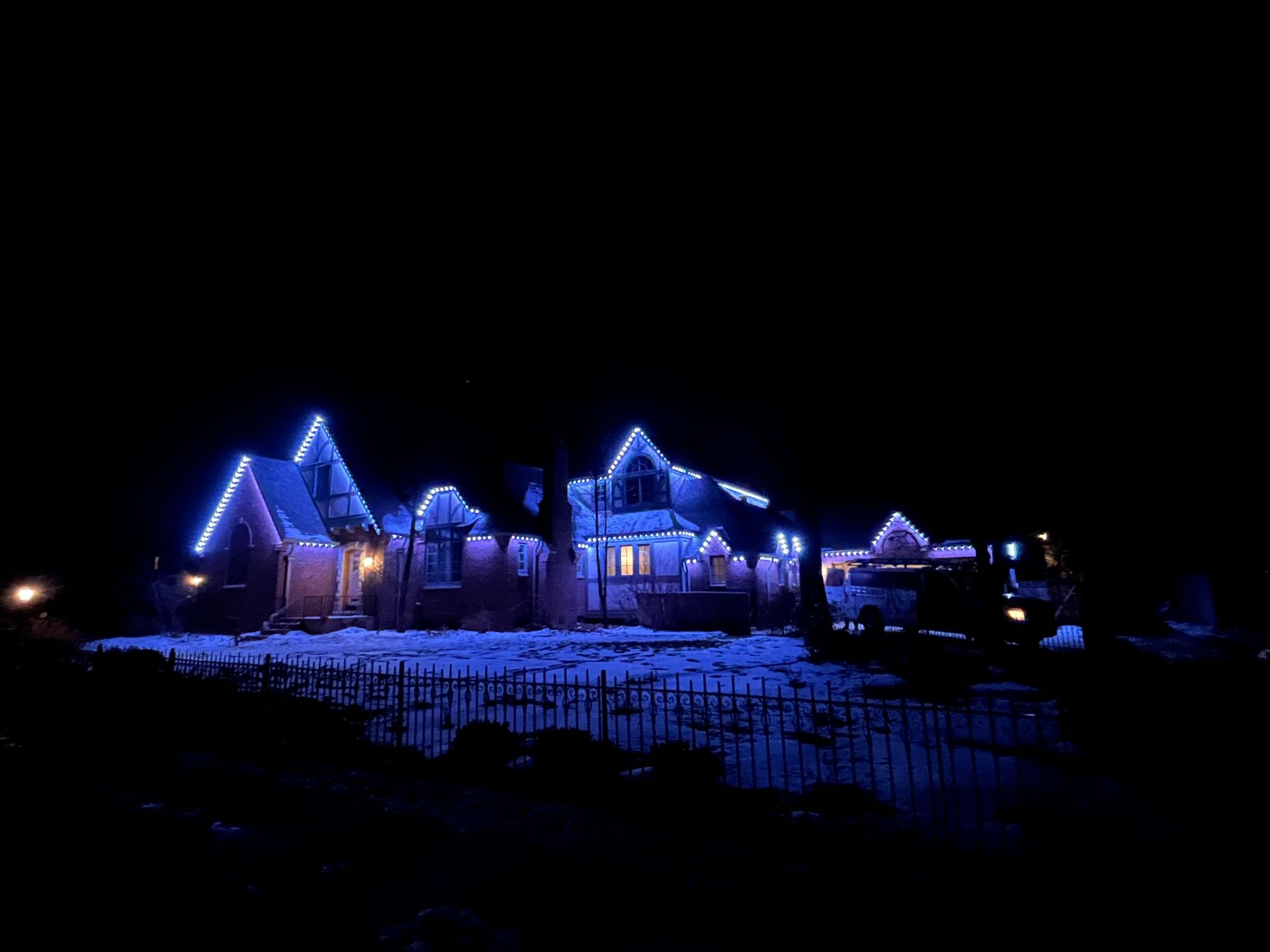Snowy houses outlined in blue lights at night on a dark hillside