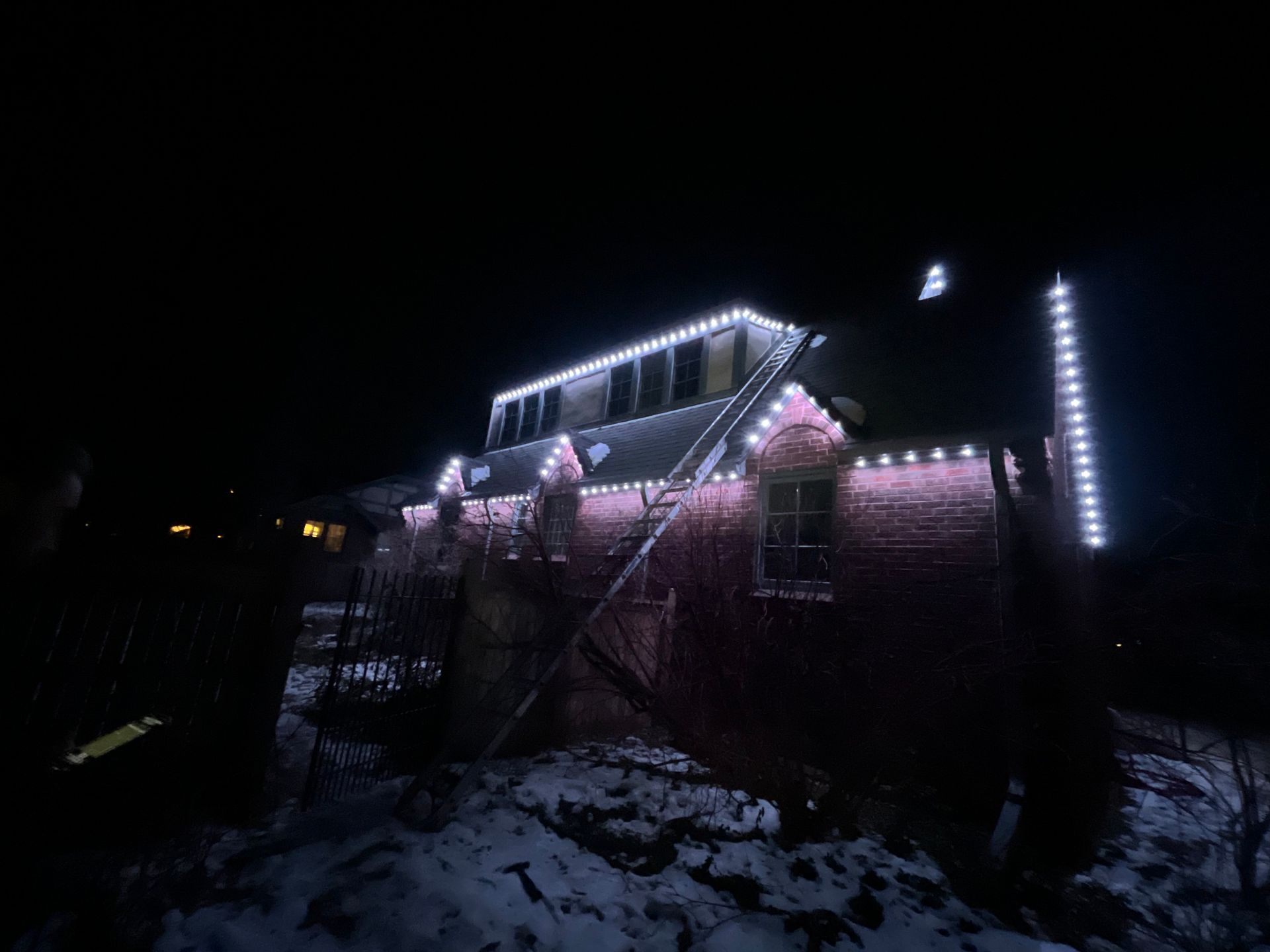 House lit with white and pink lights at night, with snow on the ground and a dark sky.