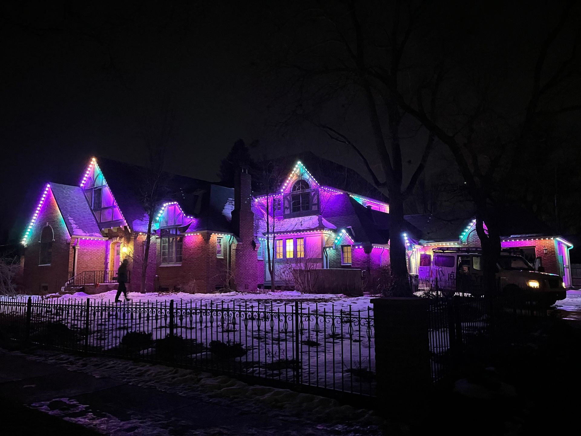 Snowy house lit with purple and pink holiday lights at night