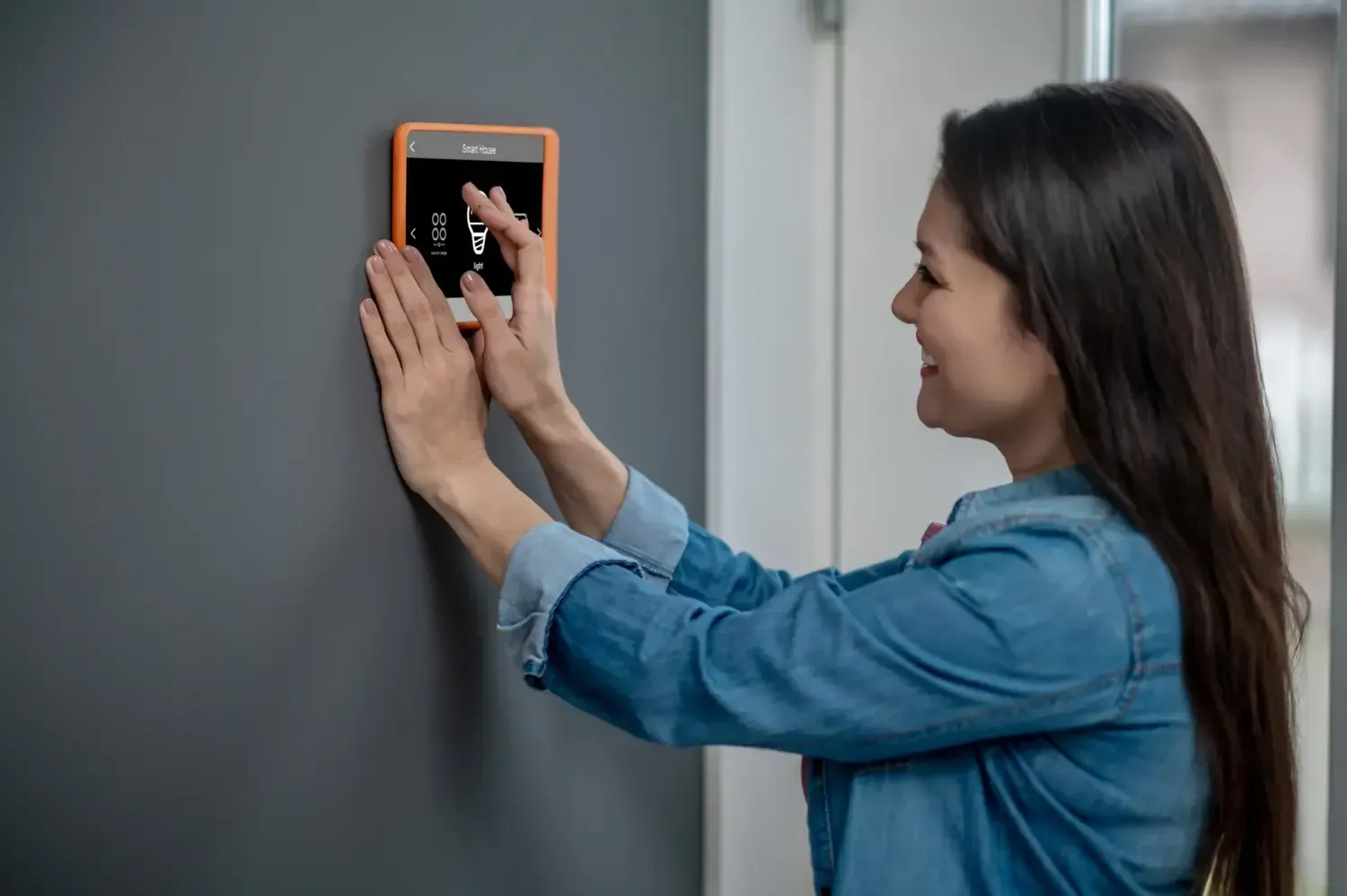 Woman using a wall-mounted thermostat with a touchscreen panel