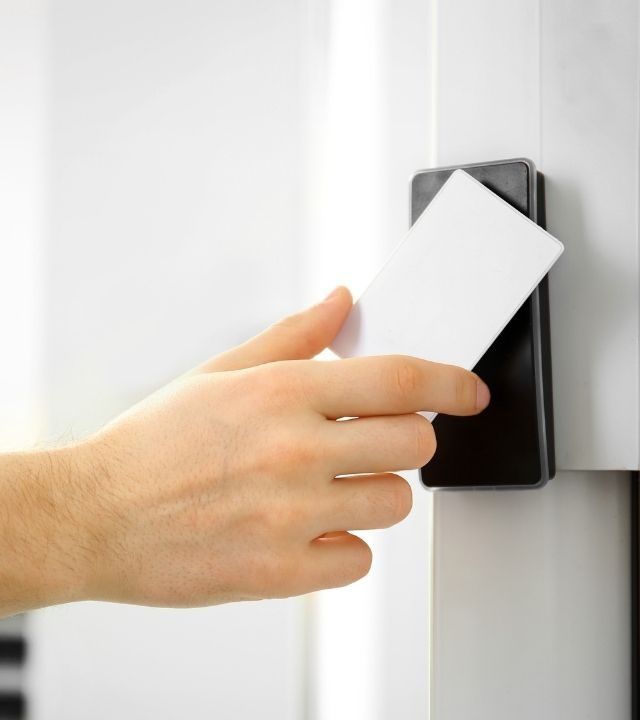 Hand holding a white card near a black card reader on a door frame