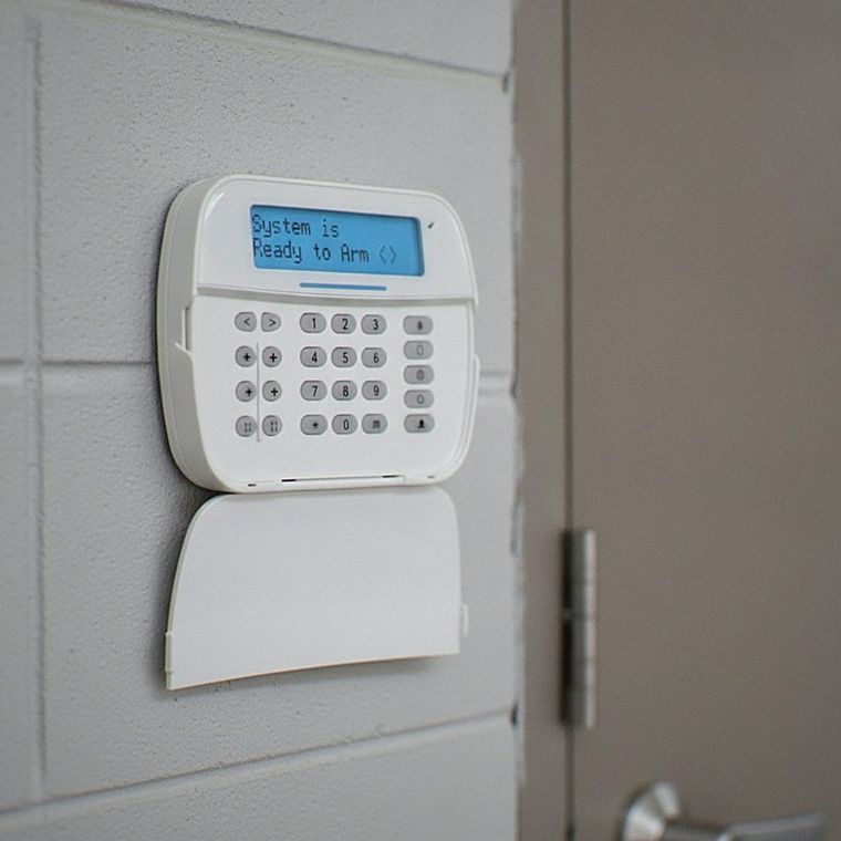 Wall-mounted security keypad with blue display and keypad above a door lock, on a gray wall