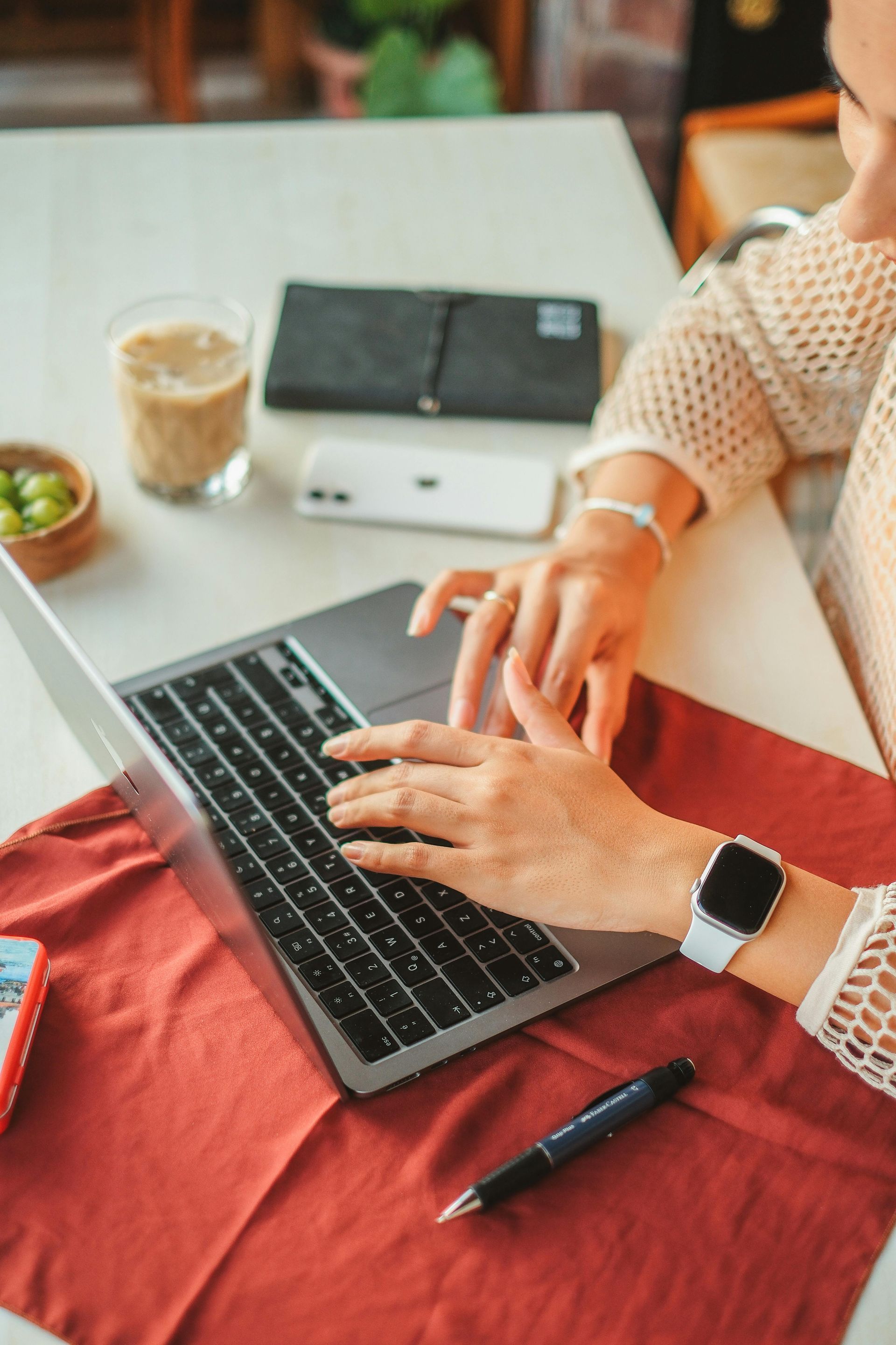 Hands typing on a laptop at a desk with coffee, notebook, and pen.