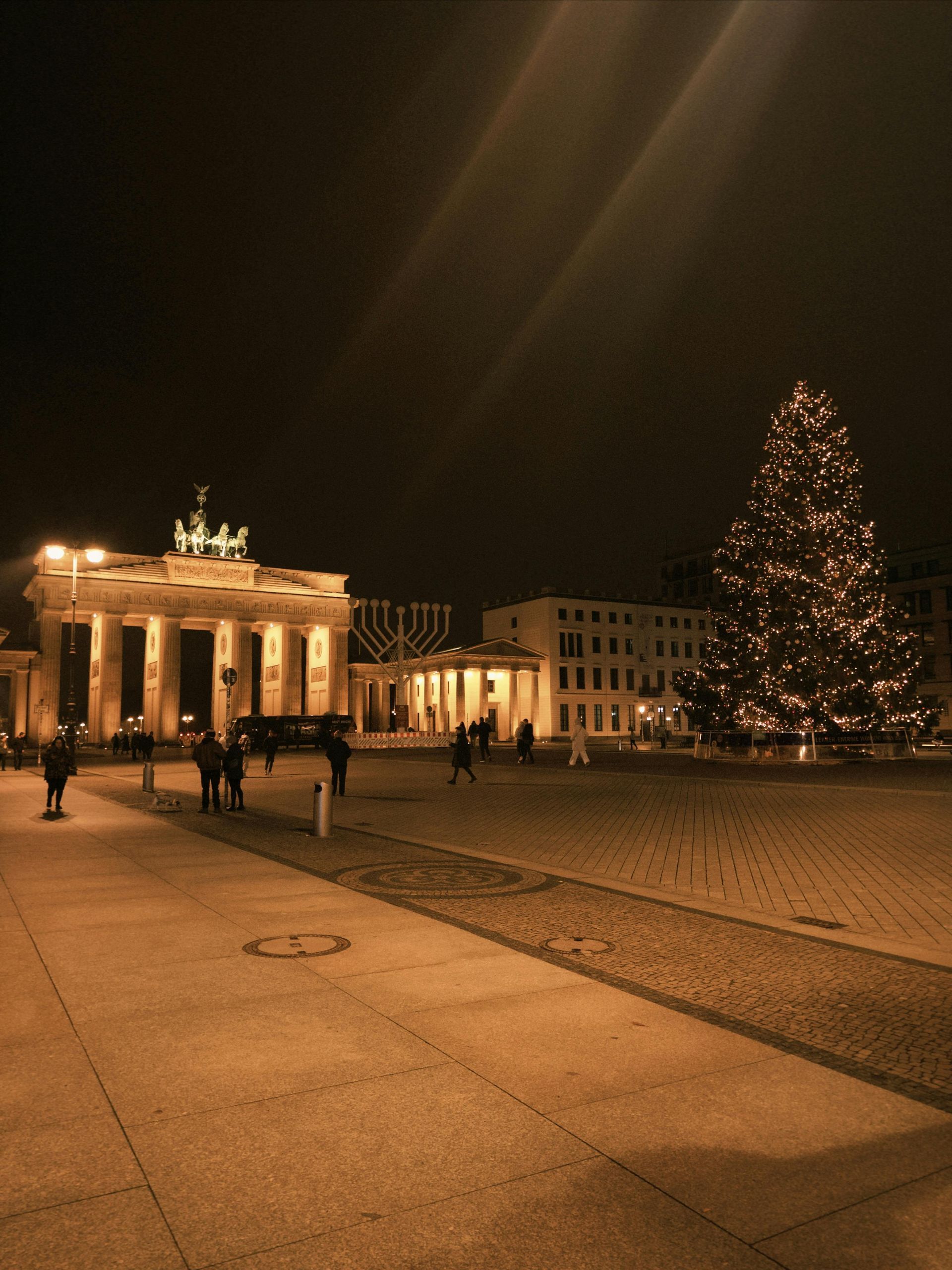 Brandenburg Gate at night with a lit Christmas tree and a few people in the plaza