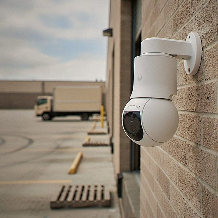White security camera mounted on a brick wall overlooking a parking lot with a truck in the distance