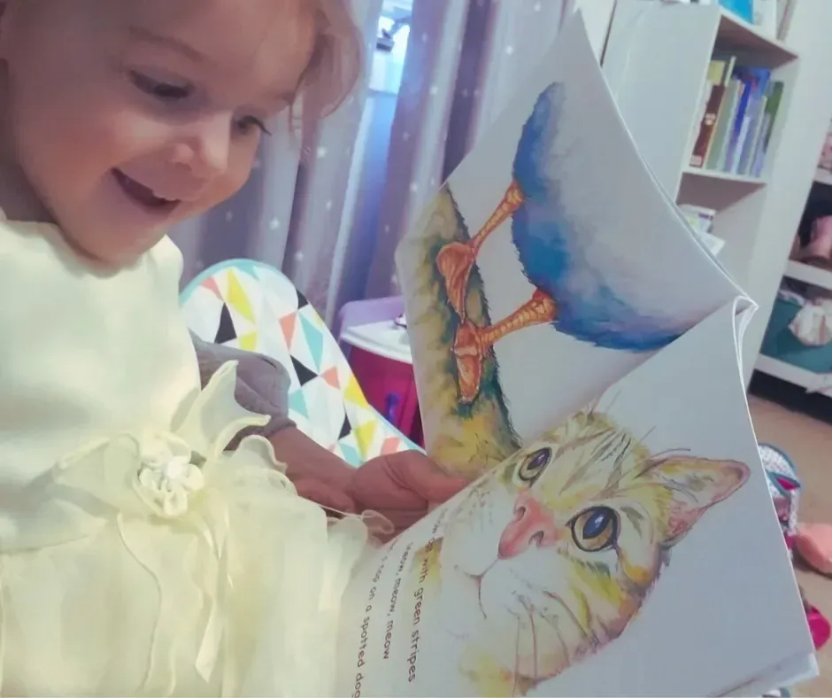Child smiling while reading a colorful bird book indoors