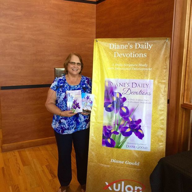 Woman holding a book beside a banner for Dianne’s Daily Devotions at a conference booth