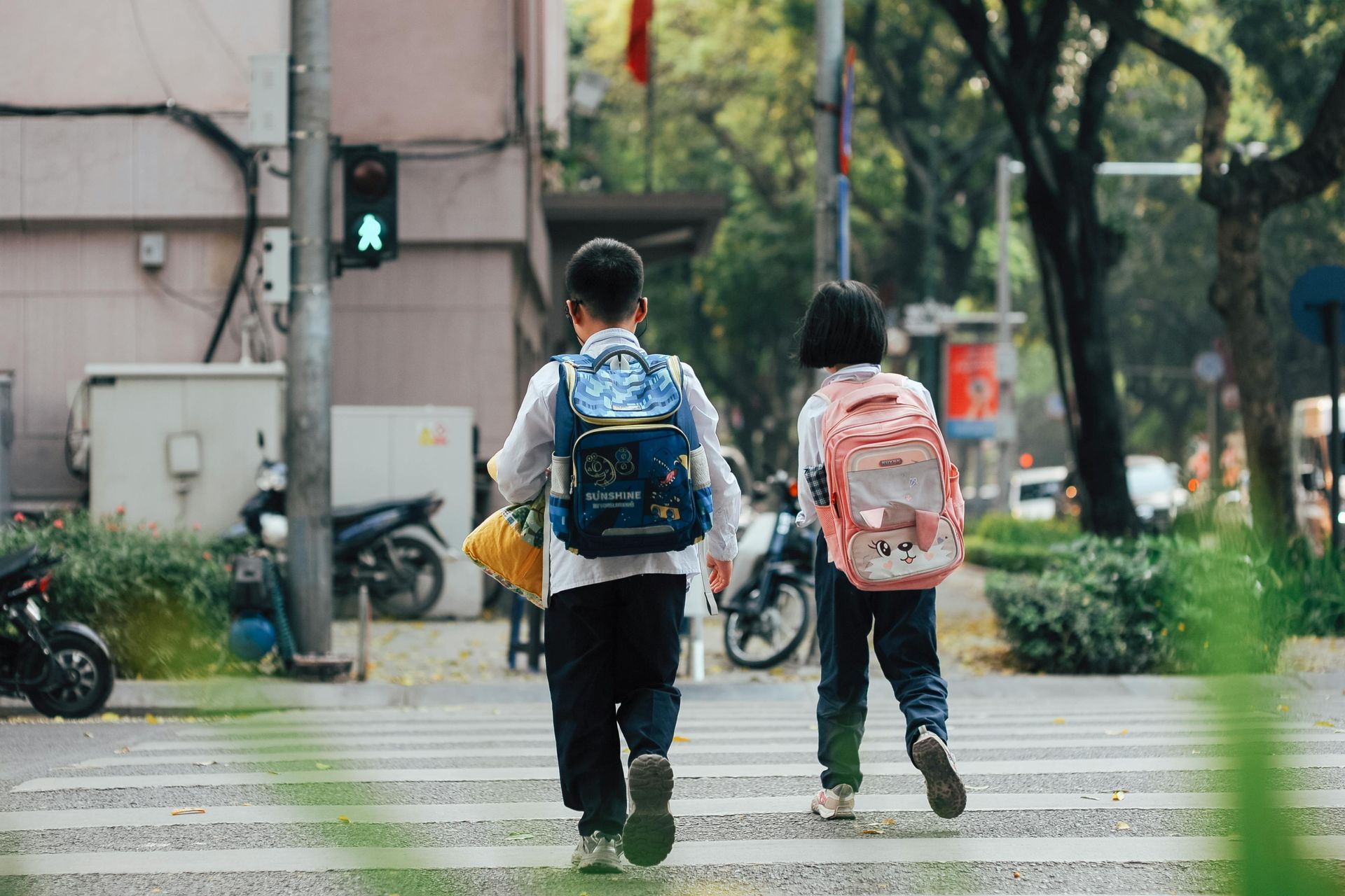 Two children with backpacks crossing a crosswalk in a city street