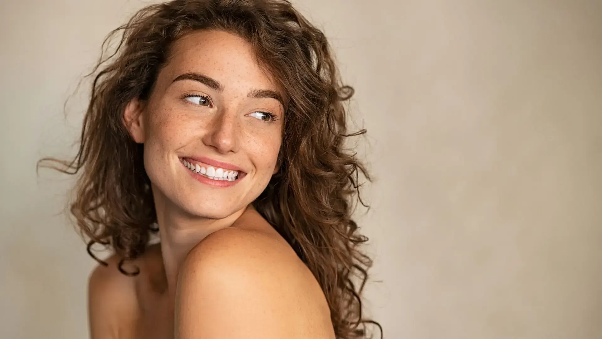 A woman with curly hair is smiling and looking over her shoulder.