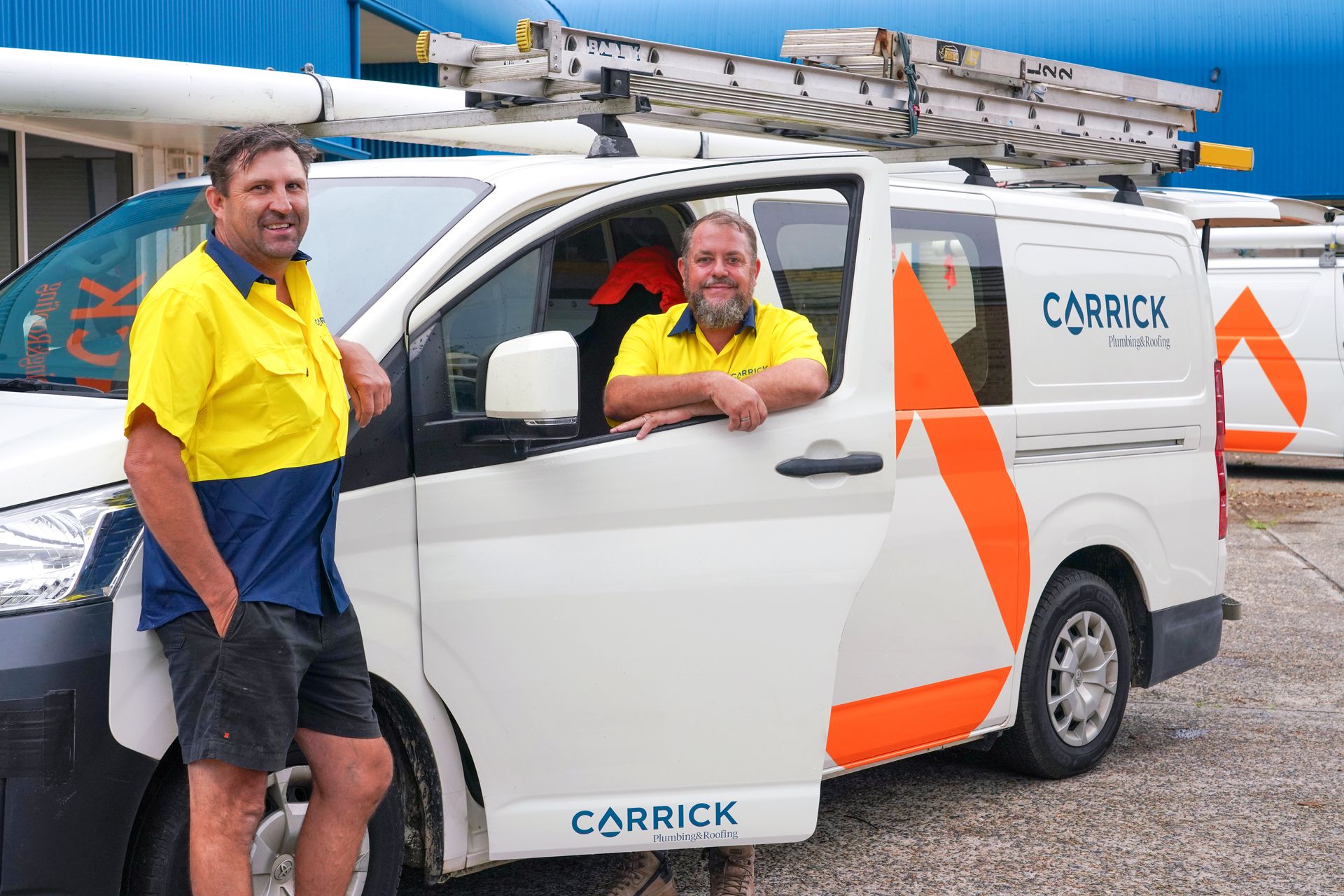 Two Carrick Plumbing team members in yellow shirts are standing next to a white van branded with Carrick Plumbing & Roofing in Port Macquarie.