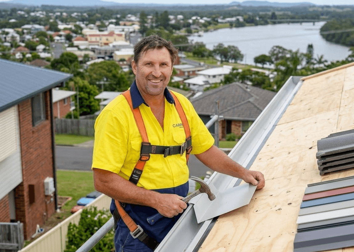 Roofer on a roof, installing gutter, safety harness. Kempsey and river in background.