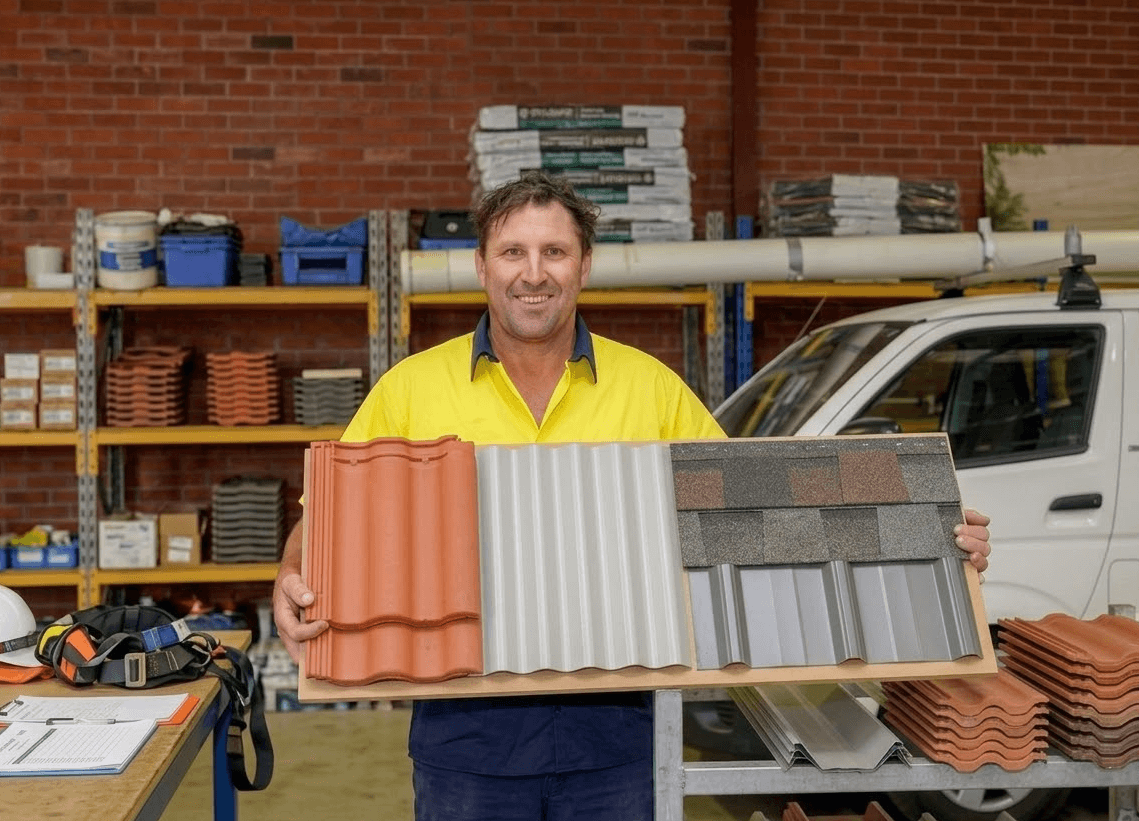 Man holding roof tile samples in a warehouse, smiling.
