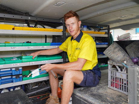 Carrick Plumbing & Roofing employee wearing yellow shirt sitting inside a van beside shelves of tools and plumbing equipment.