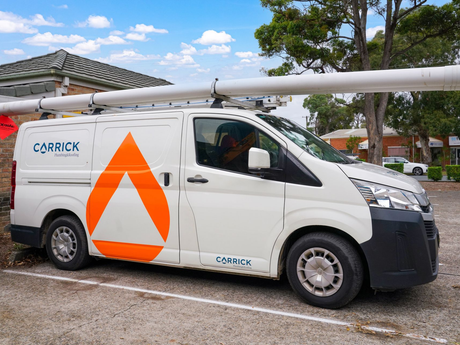 Carrick Plumbing branded white van with an orange triangle on the side is parked in a parking lot ready for dispatch.