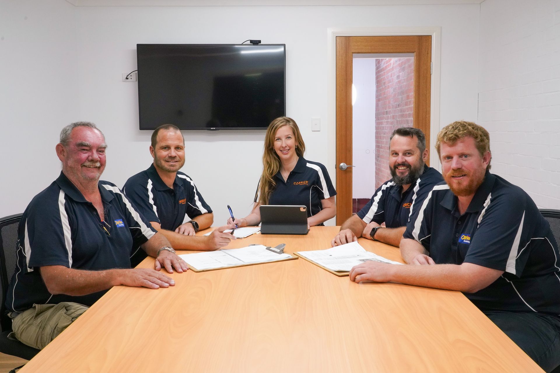 Carrick plumbing team members in matching shirts sit around a table in an office, discussing documents.