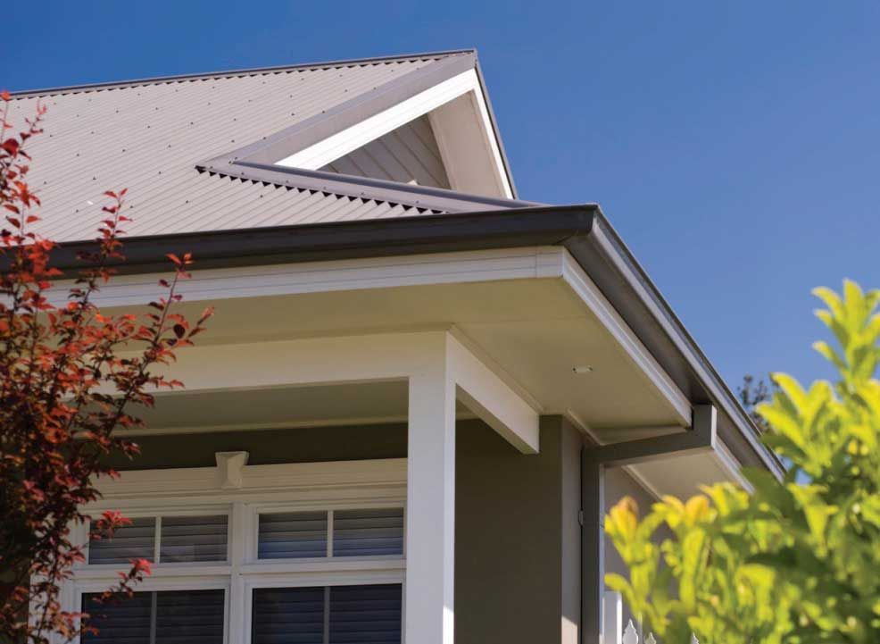 House colorbond roof and front porch against a blue sky, with a tree branch in the foreground