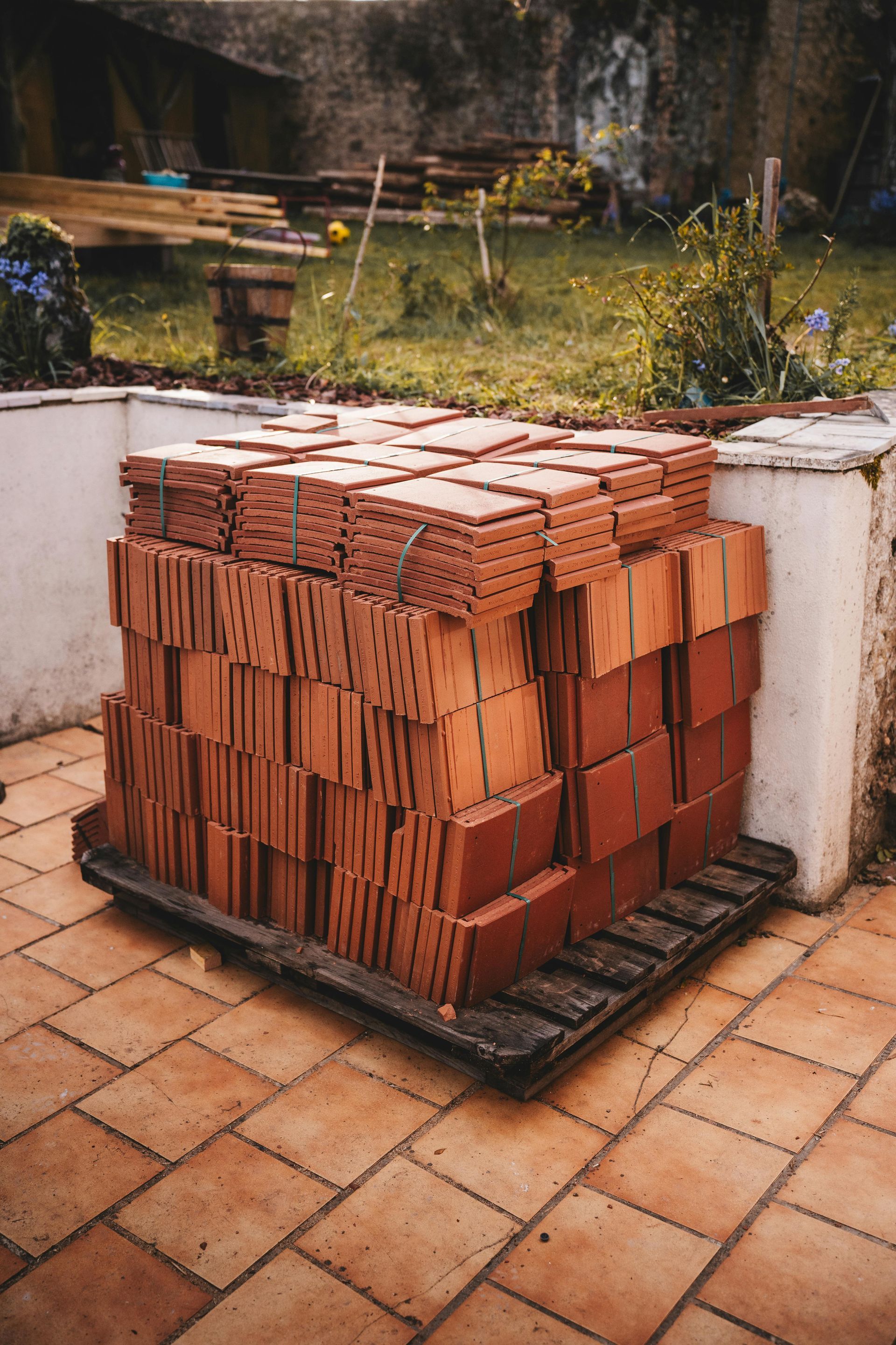 Stack of red tile bricks on a pallet, resting on a tiled patio.