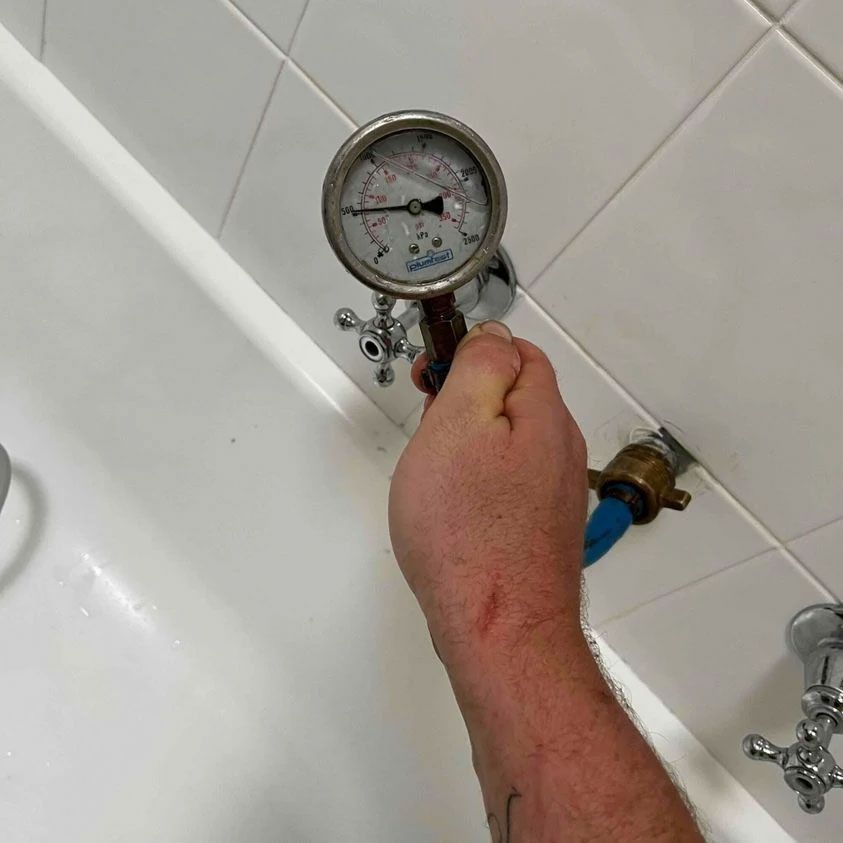 A person is holding a pressure gauge over a bathtub to check the hot water pressure