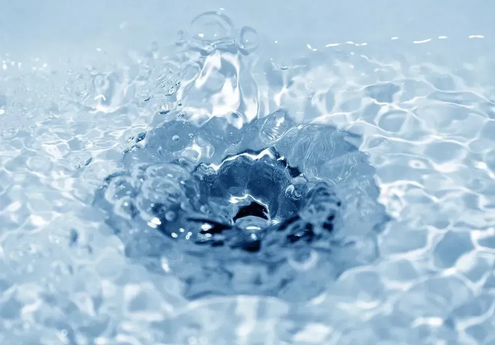 A close-up view of clear, blue water rippling outward from a central point as a drop splashes into the surface.
