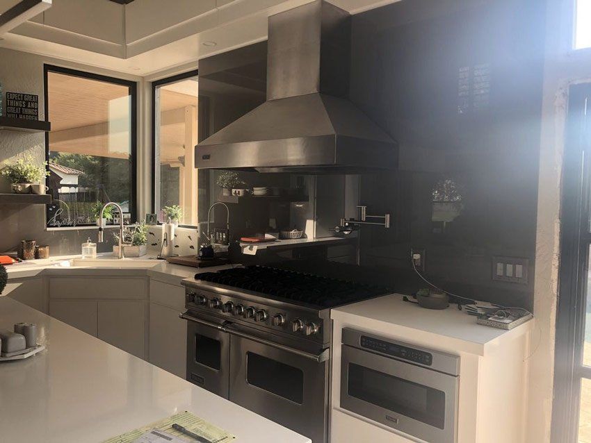 Modern kitchen with gray cabinets, stainless steel range hood, oven, and a sunlit window.