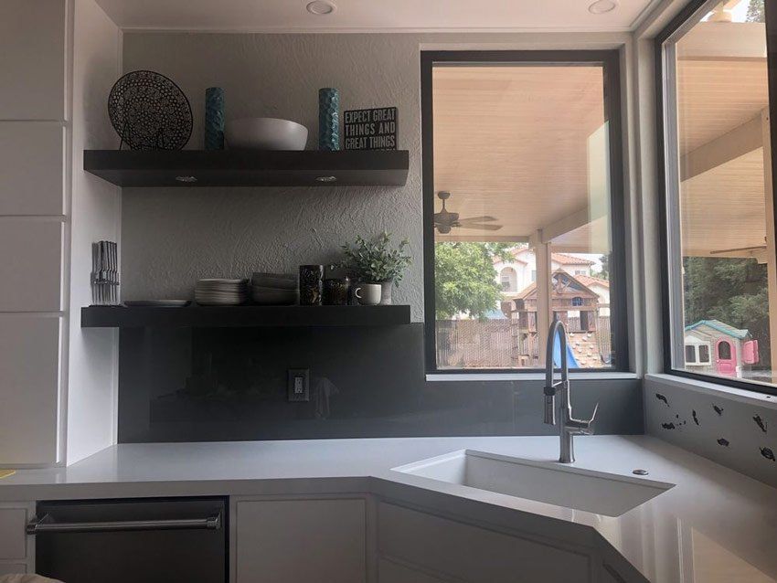 Modern kitchen sink area with dark shelves, white countertop, and large window view outside