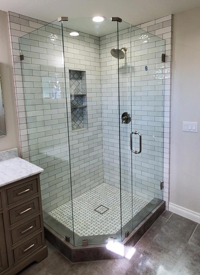 Corner glass shower enclosure with white subway tile and gray hex tile floor in a modern bathroom