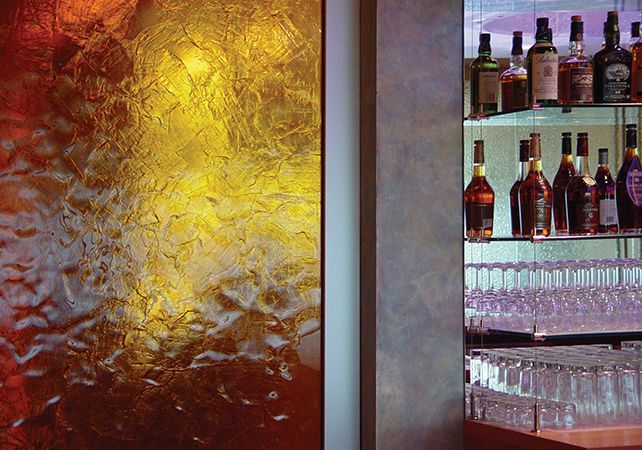 Bar with frosted glass panel and illuminated shelves of liquor bottles and glasses