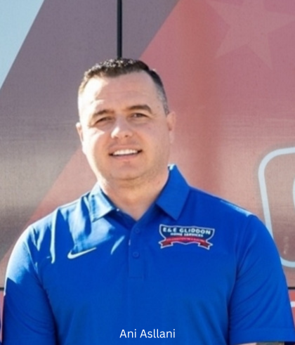 Man in a blue polo shirt standing outdoors in front of a maroon wall, smiling
