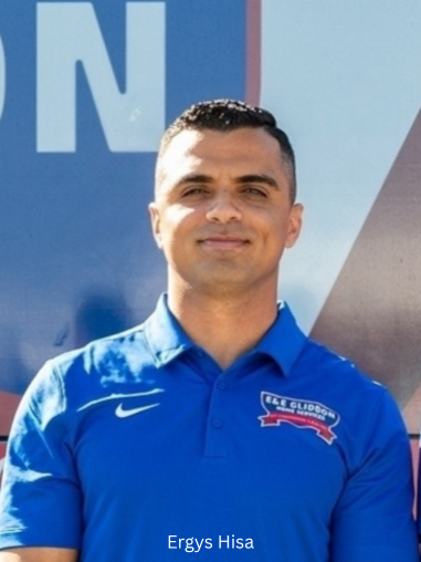 Man in blue polo shirt standing in front of a blue backdrop, smiling at the camera.