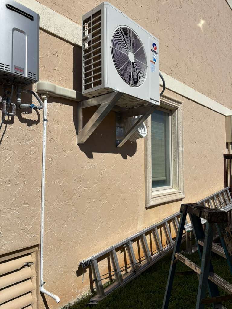 Two white outdoor heat pump units beside a gray house on gravel, next to a green lawn.