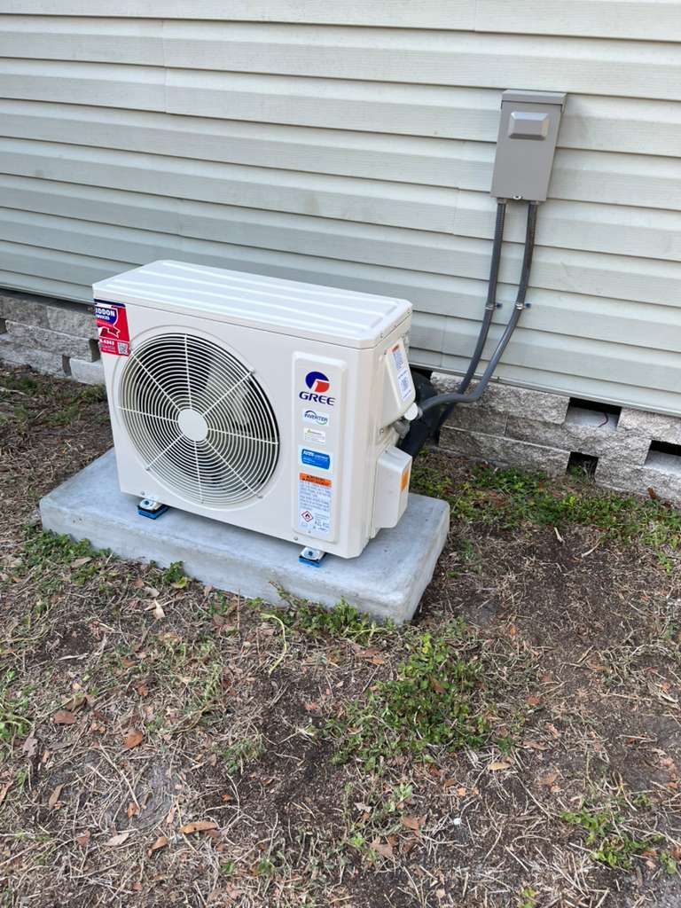 Outdoor AC unit with technician in red working beside it in a grassy yard