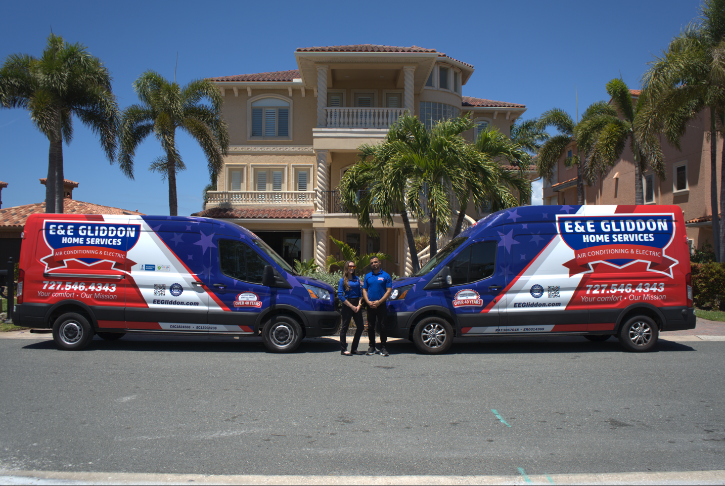 Two red-and-blue service vans parked side by side in front of a large house with palm trees