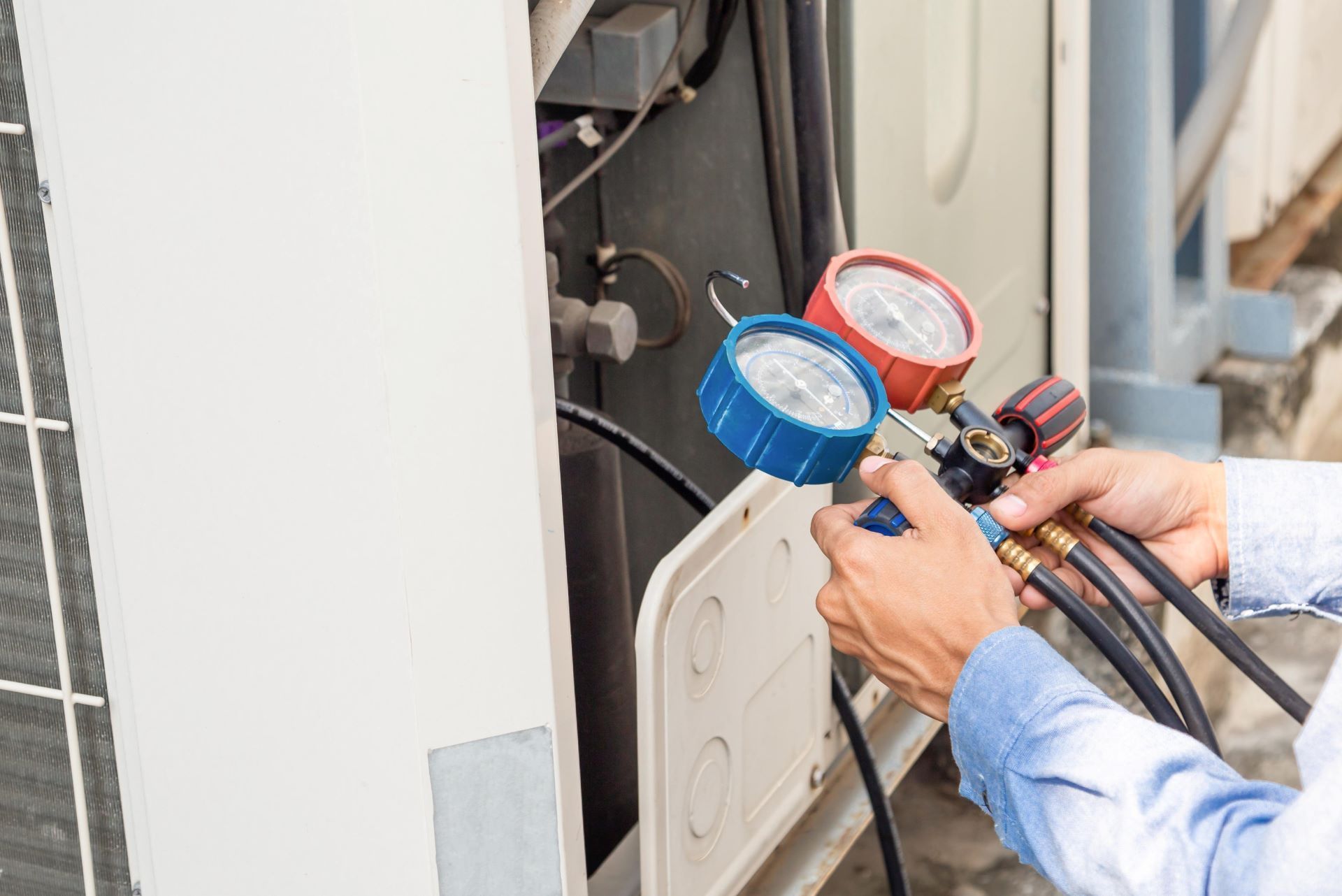 Technician connecting blue and red gauges to an outdoor HVAC unit for maintenance