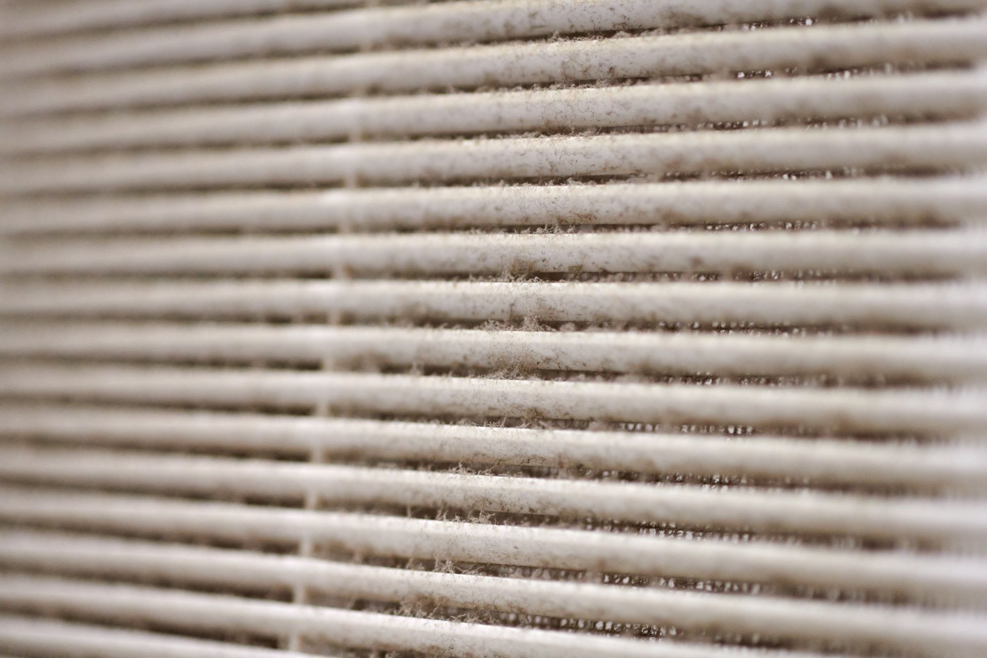 Hand holding a curved air filter beside an air conditioner vent indoors