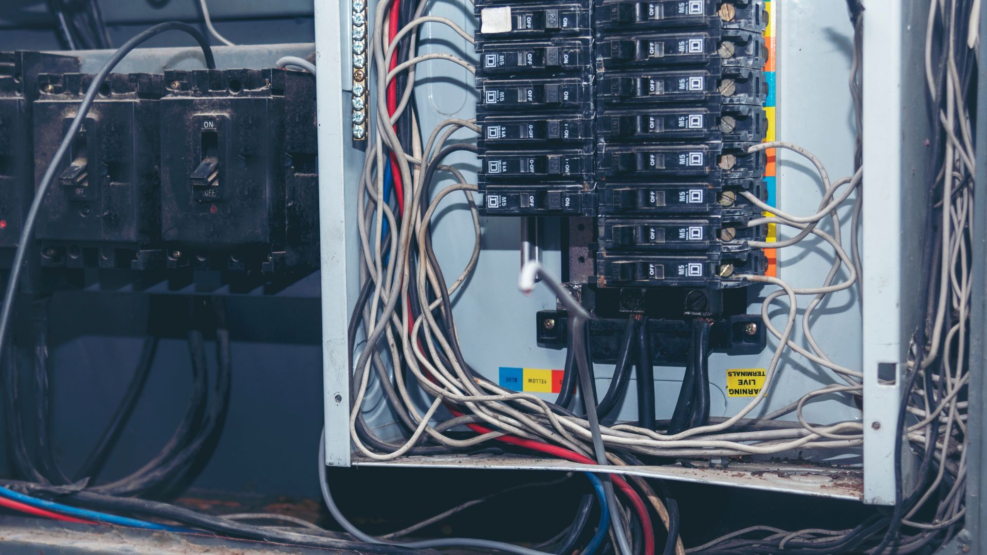 Electrical panels with rows of circuit breakers and tangled wiring in a utility room
