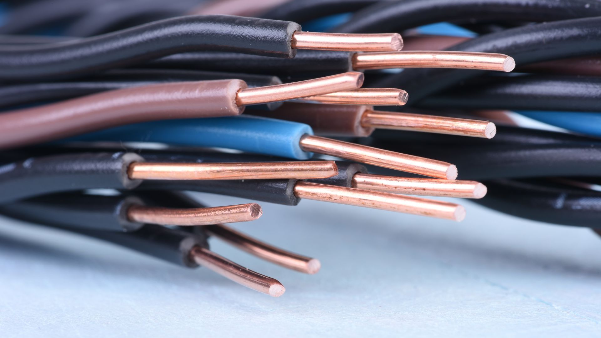 Close-up of stripped electrical wires with exposed copper ends in black, brown, and blue insulation.