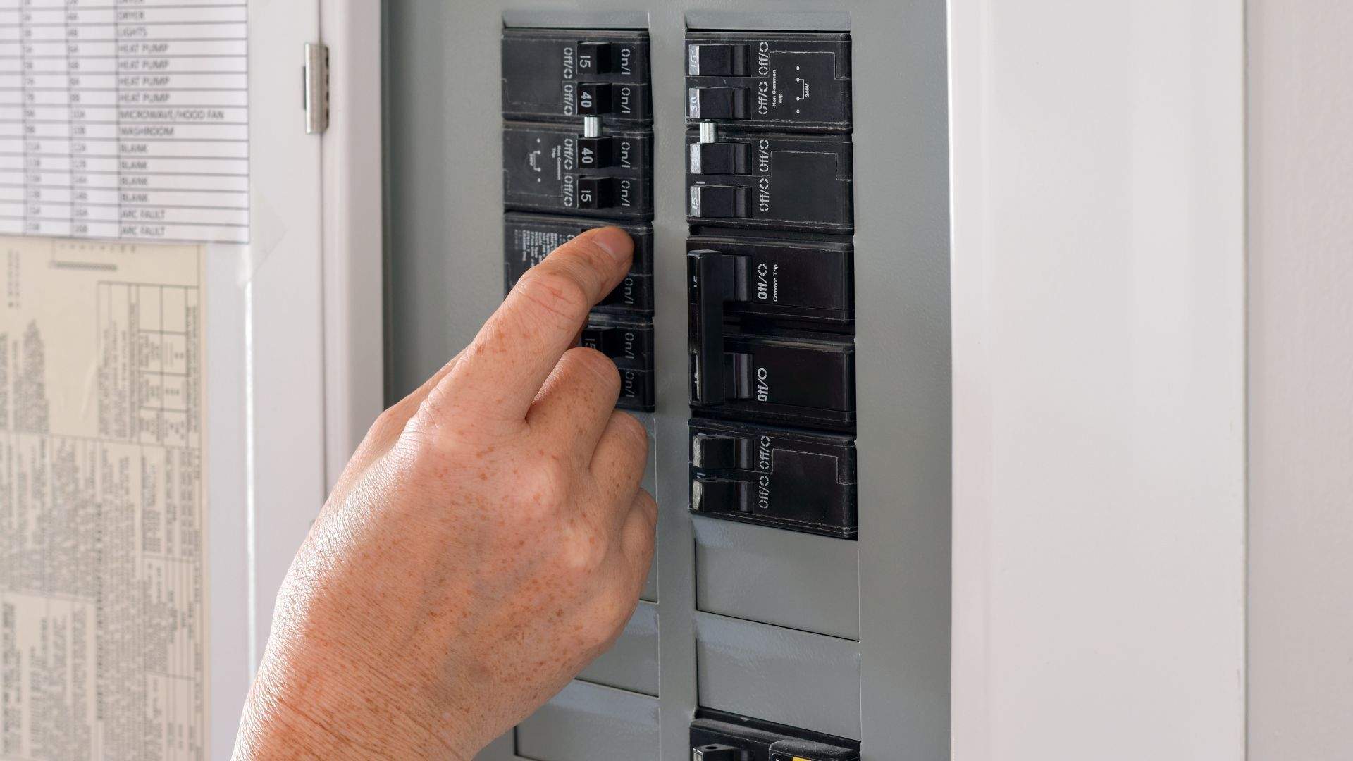 Hand turning on a breaker switch in an electrical panel near a window