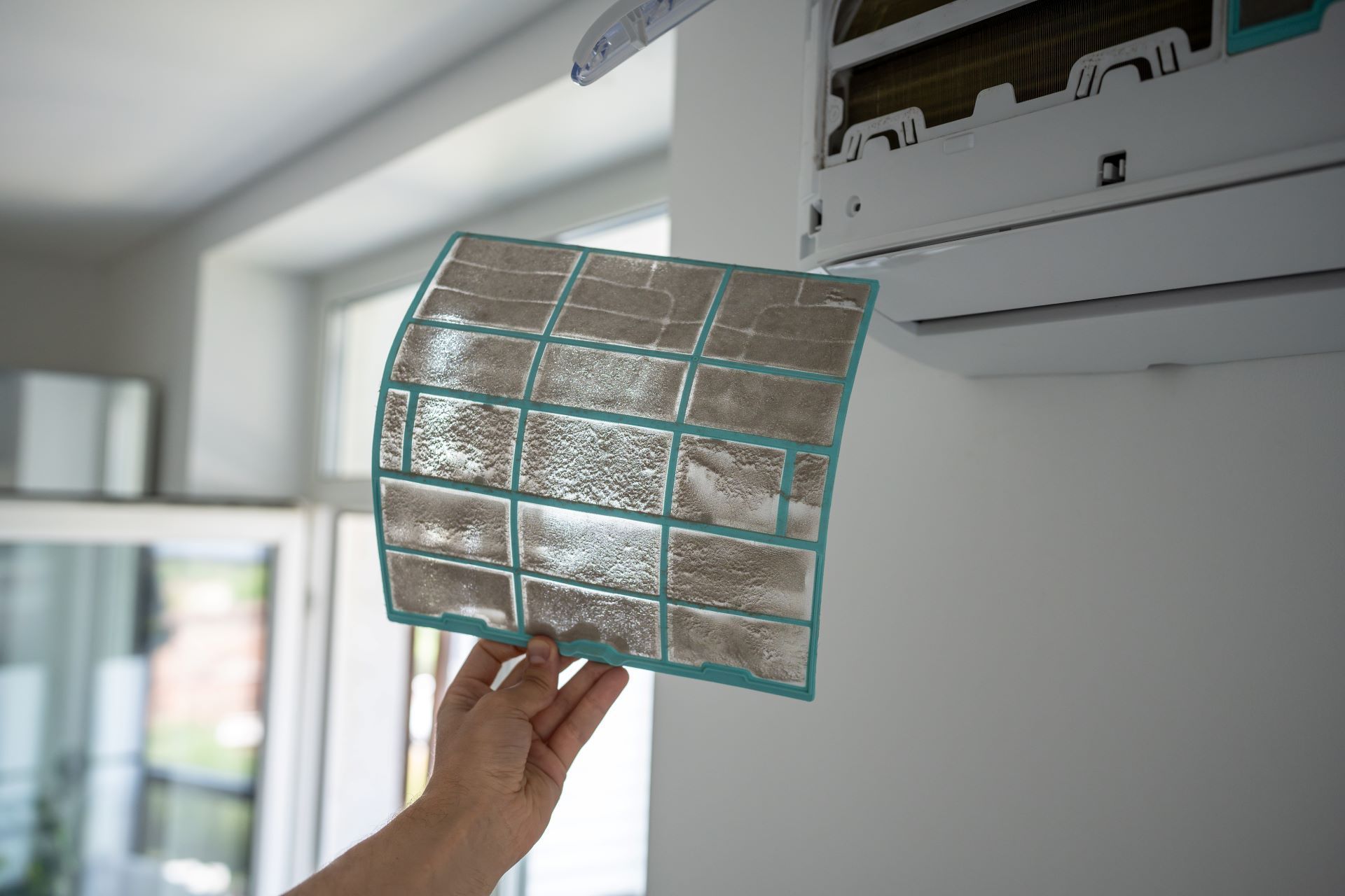 Hand holding a curved air filter beside an air conditioner vent indoors
