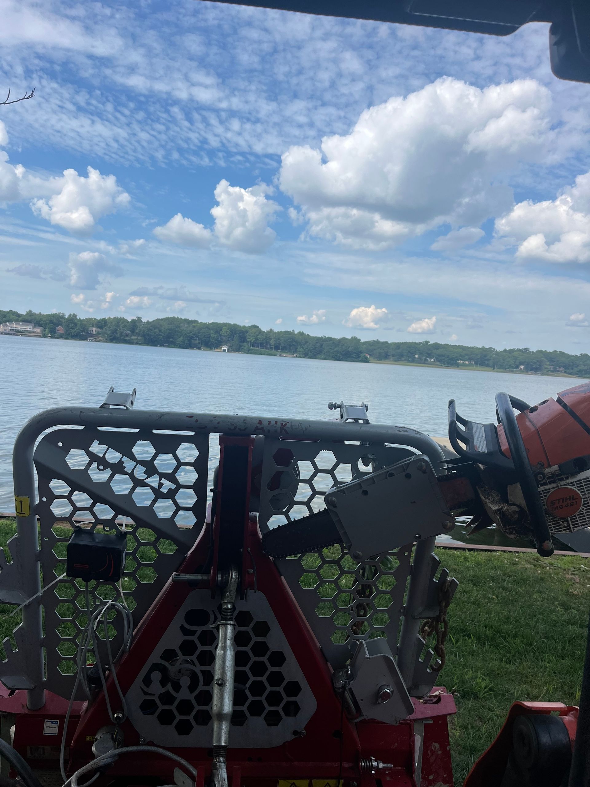 View from a machine overlooking a lake on a sunny day, with blue sky and clouds.