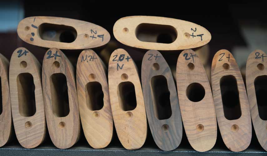 Wooden gun stocks, some labeled with numbers and letters, arranged in a row.